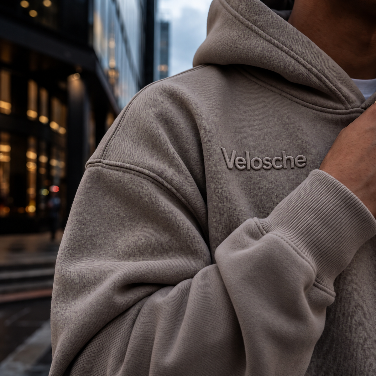 Close view of a taupe Velosche hoodie on a city street at dusk